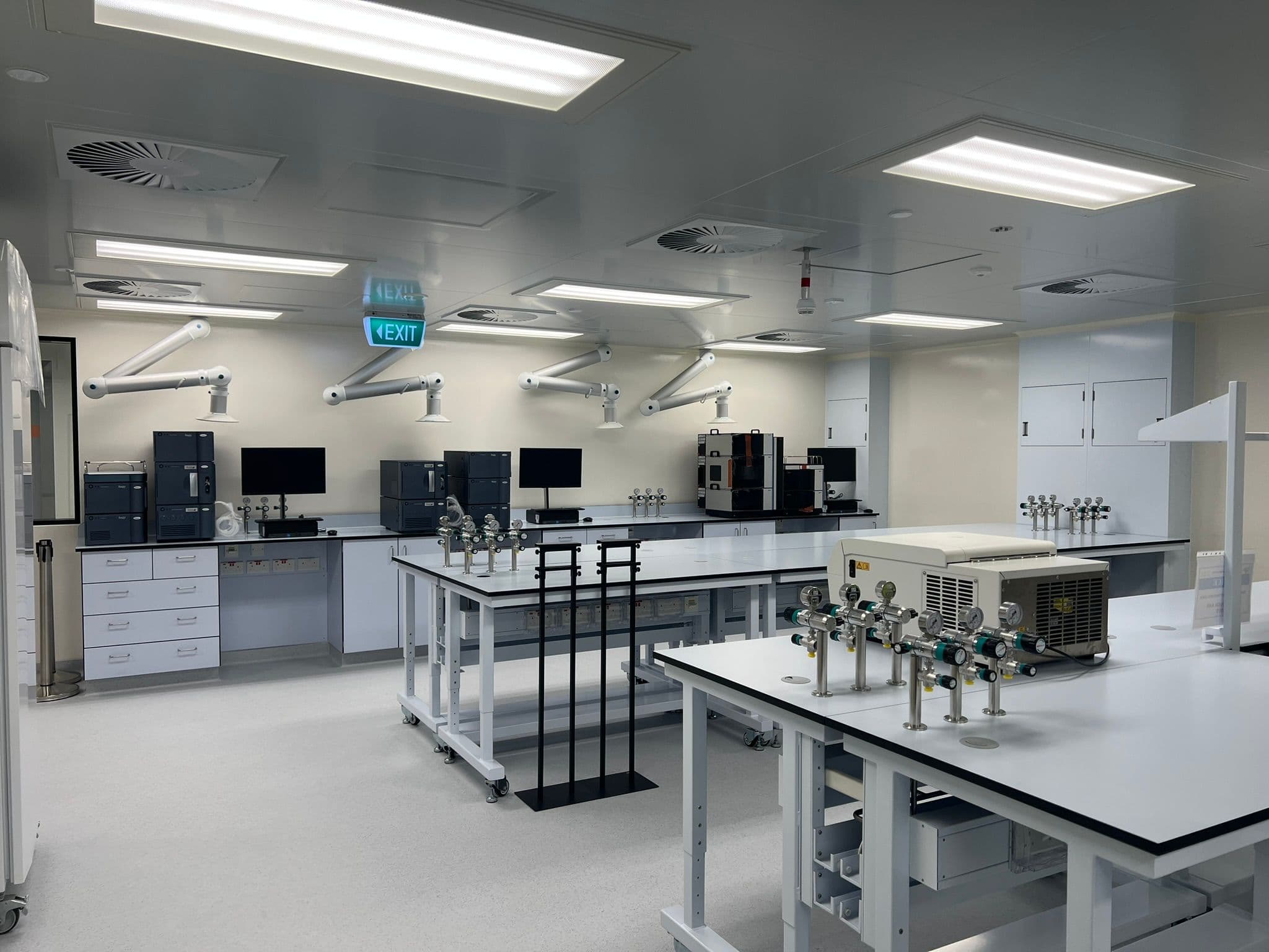 Quality-control laboratory with workbenches, monitors, extraction arms, and ceiling services.