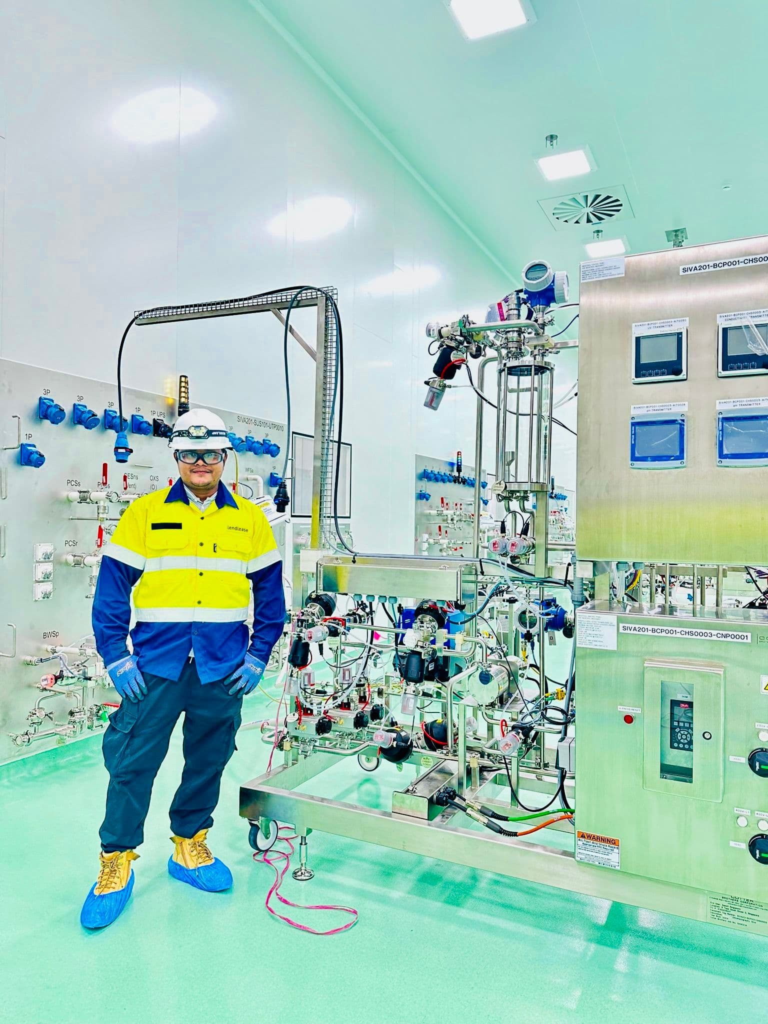 Engineer standing beside stainless-steel process equipment and piping in a clean production area.